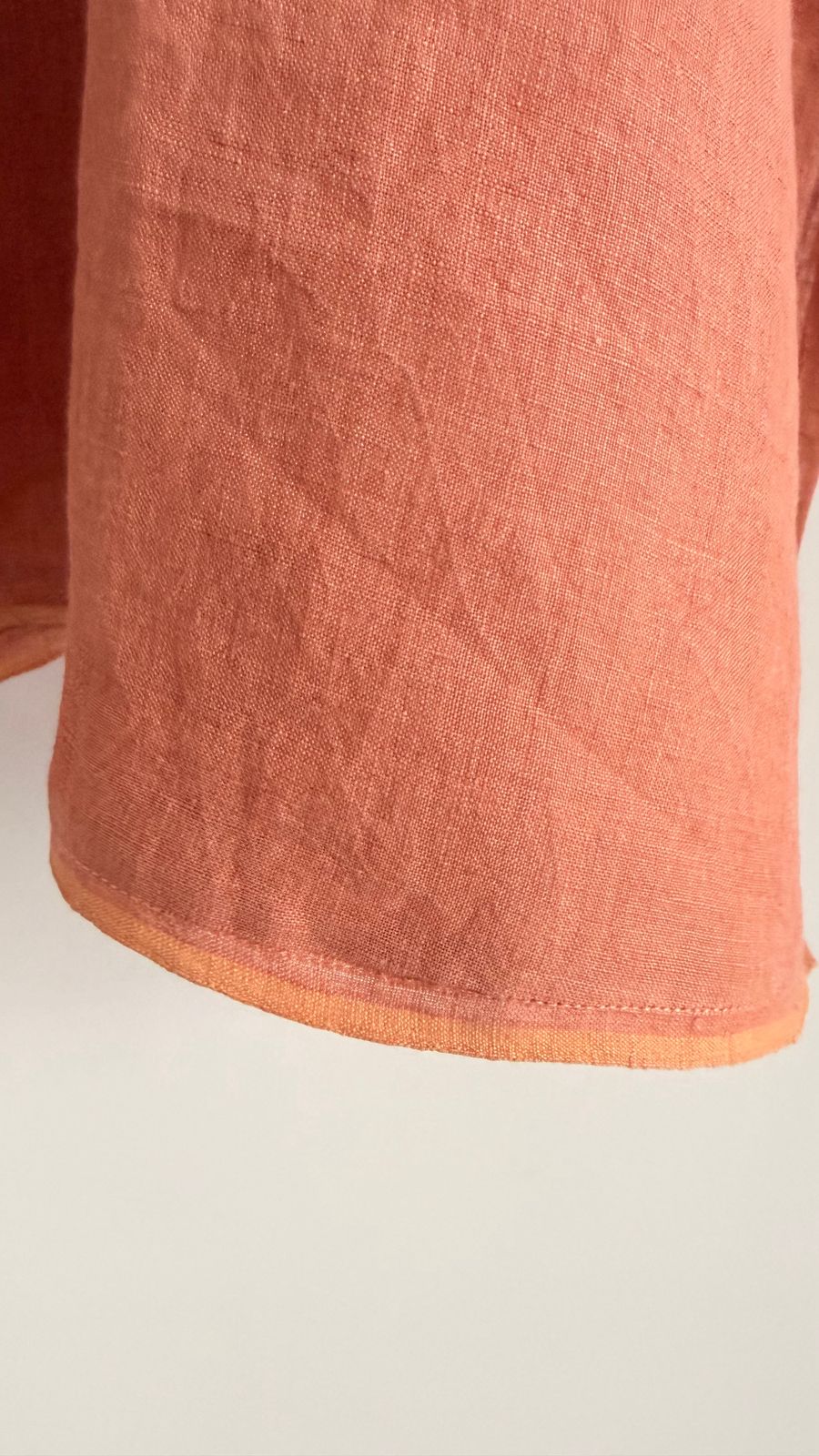 Close-up of breathable tangerine linen fabric showing natural texture and subtle hem finish