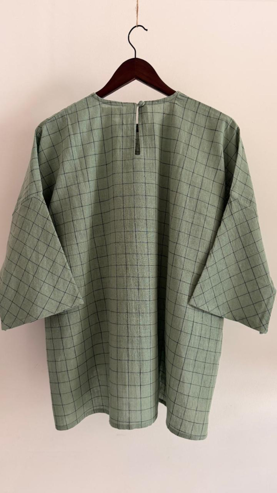 Back view of pale teal handwoven cotton top with grid weave, wide sleeves, and button closure.