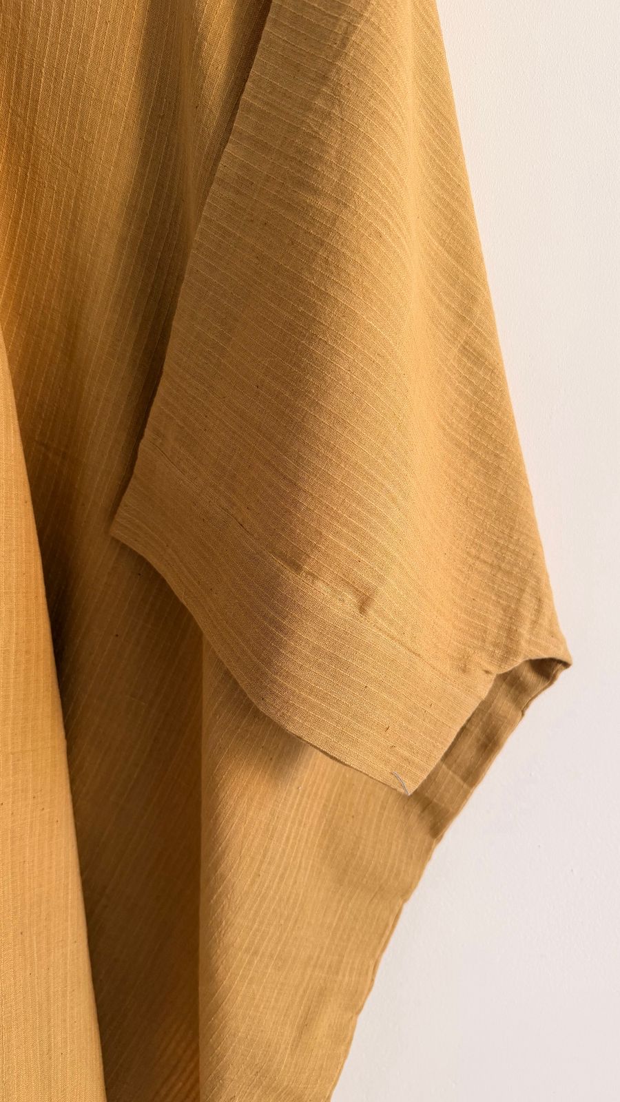 Close-up of the Sage Kaftan in ochre handwoven khadi, showing the bark-toned border and relaxed sleeve detail.