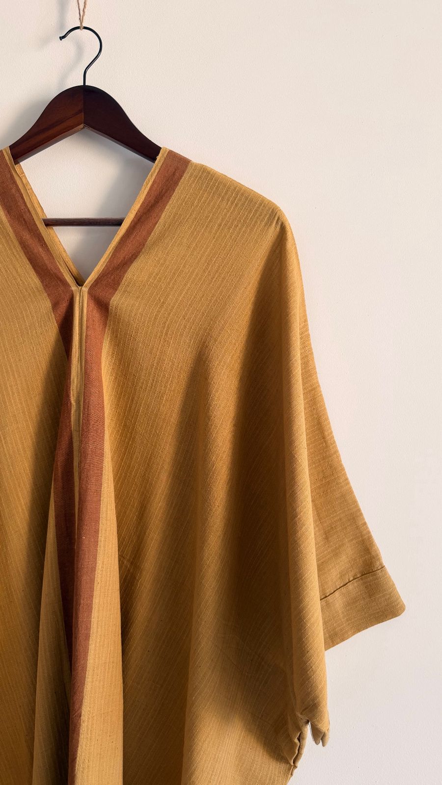 Handwoven Sage Kaftan in ochre with bark brown neckline border hanging on wooden hanger