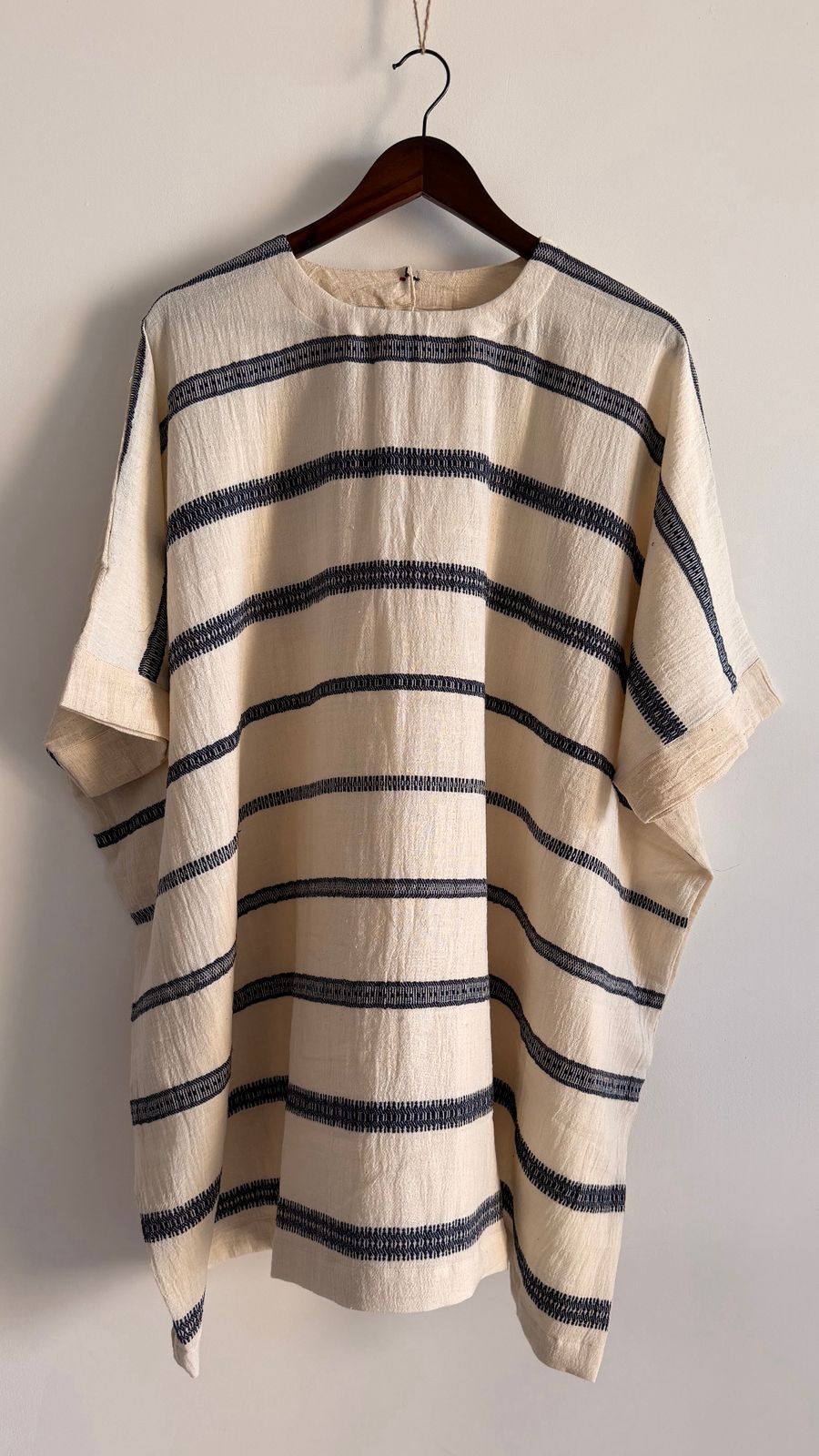 Full view of Cedar Dress in ivory ink striped handwoven cotton, relaxed silhouette hanging on wooden hanger