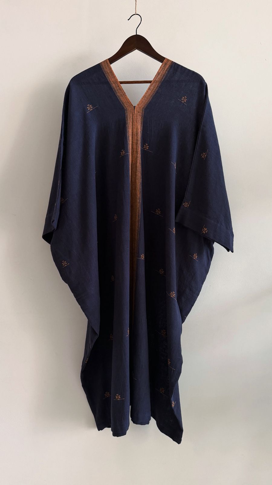 Navy handwoven kaftan with amber woven border along the neckline and edges, featuring small geometric motifs scattered across the fabric.