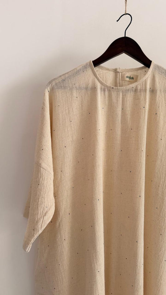 Close-up of handwoven cotton dress in kora with scattered ink-speck detailing, round neckline, and soft natural texture.