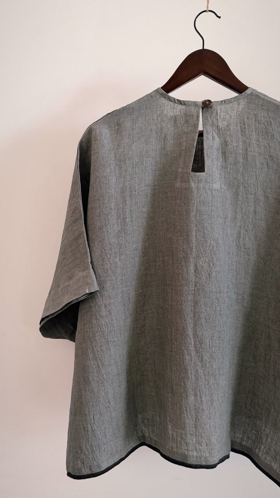 Back view of the Elm handwoven linen top in ash grey, featuring a keyhole button closure and black contrast hem.