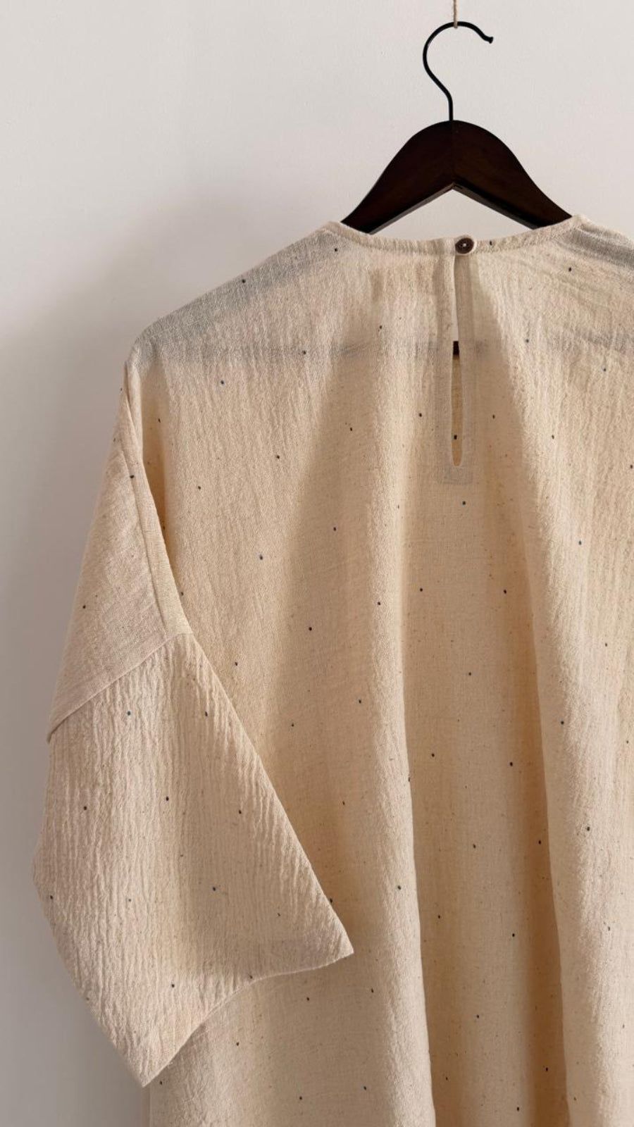 Back view close-up of handwoven kora cotton dress with ink-speck weave, featuring a small button closure and slit opening.