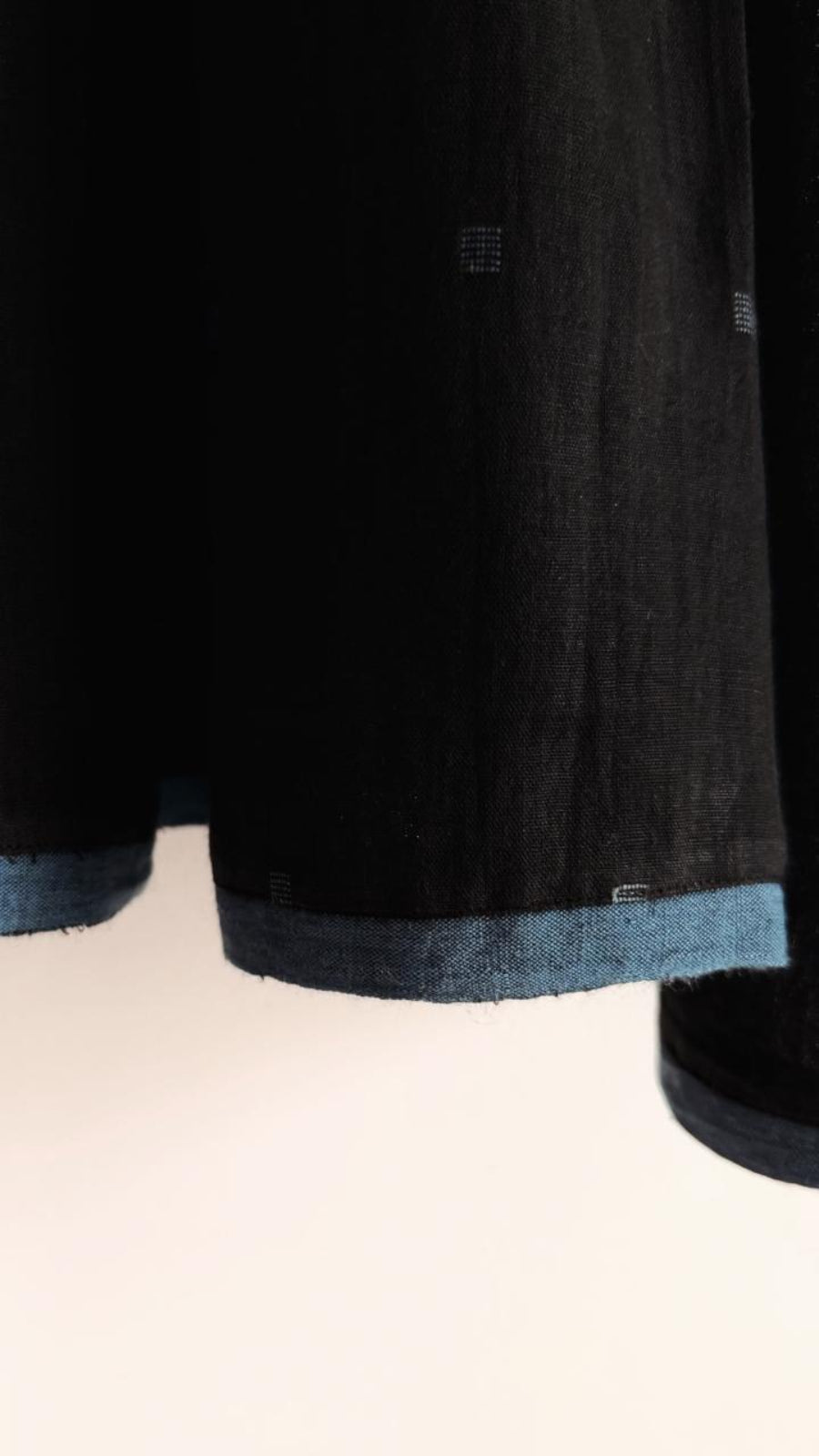 Close-up of Coal Sky khadi fabric showing Jamdani motifs and blue hem edging.