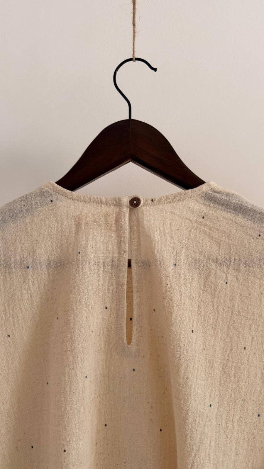 Detailed back neckline of handwoven cotton dress in kora, showing button fastening and subtle ink-speck texture.