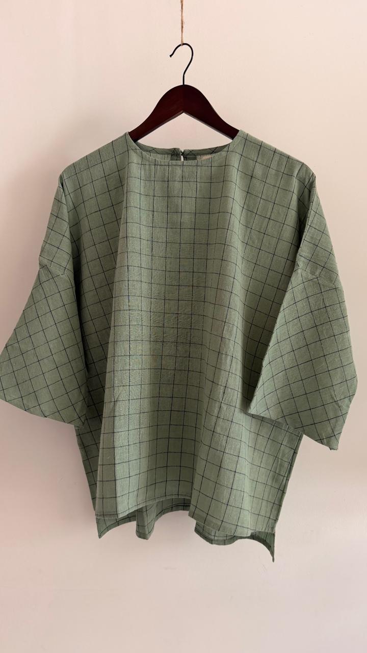 Front view of handwoven cotton top in pale teal with fine dark grid detailing, relaxed silhouette, and wide sleeves.