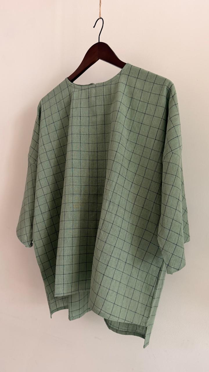 Angled view of relaxed handwoven pale teal cotton top showing fine grid detailing and wide sleeve drape.