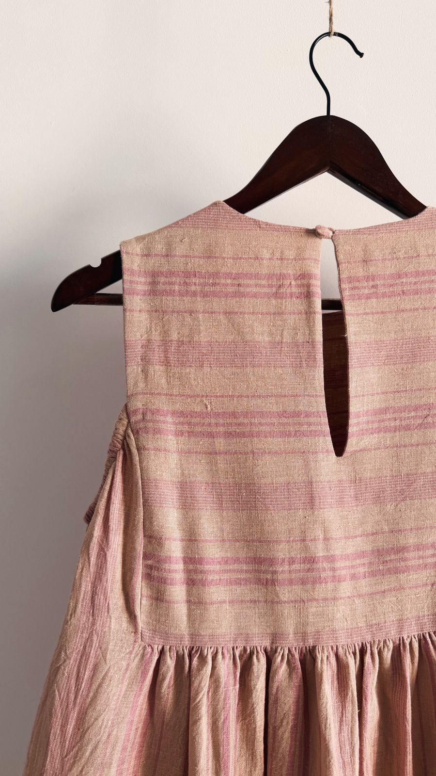 Handwoven pink striped dress with shoulder cut-out detail on wooden hanger.