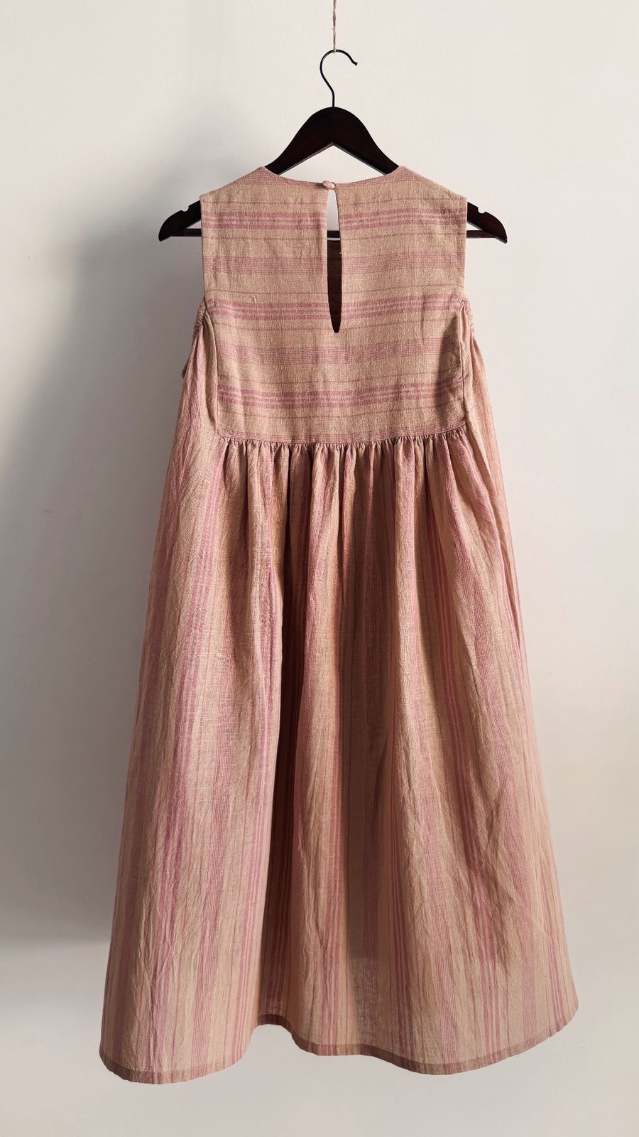 Handwoven pink striped dress with shoulder cut-out detail on wooden hanger.