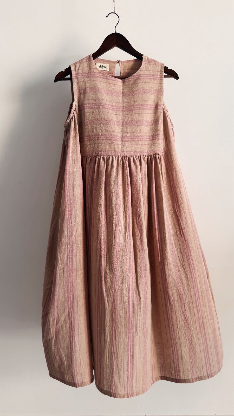 Handwoven pink striped dress with shoulder cut-out detail on wooden hanger.