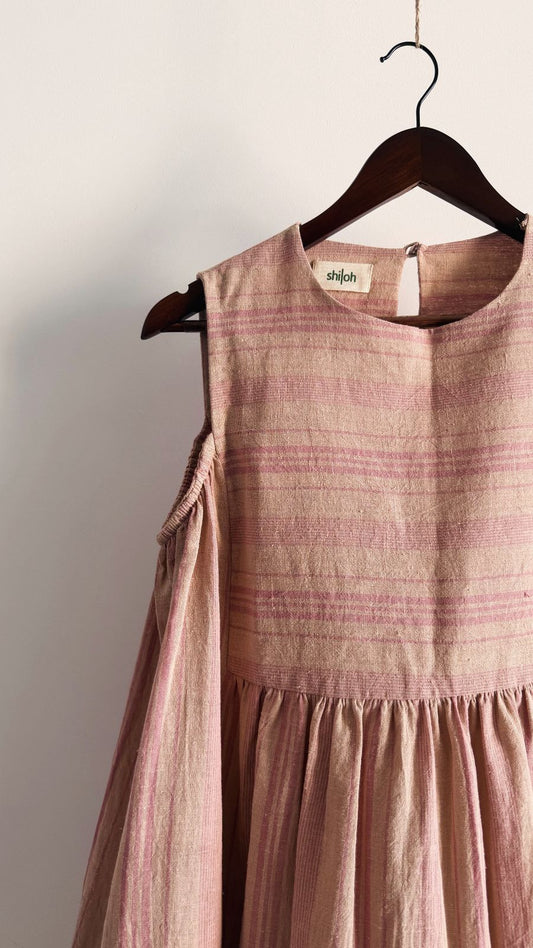 Handwoven pink striped dress with shoulder cut-out detail on wooden hanger.